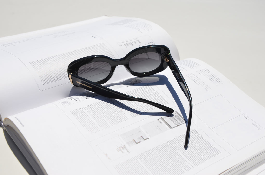 Rounded black sunglasses arms folded on top of book