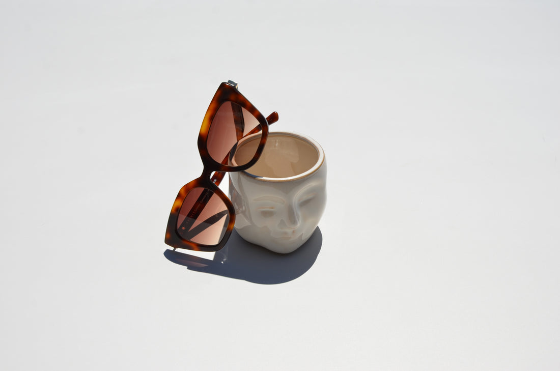 Brown sunglasses folded up leaning against white flower pot with face