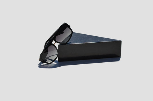 Durable black sunglasses with grey lenses propped against black triangular rock