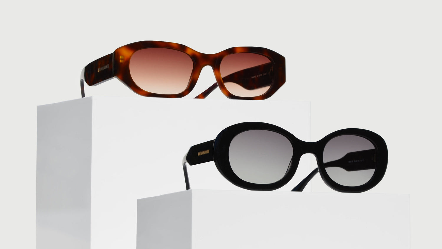 Two sleek eyewear on white pedestals. The top pair features a slim Havana brown rectangular frame, the bottom pair has a black oval frame for a minimalist look.