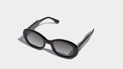 Angled front view of black oval frame sunglasses with grey oval lenses