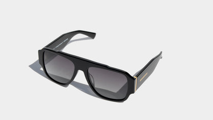 Angled front view of shiny black bold oversized shield frame sunglasses with grey square lenses