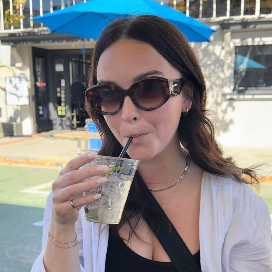 Woman wearing 2025 designer eyewear outside enjoying beverage.