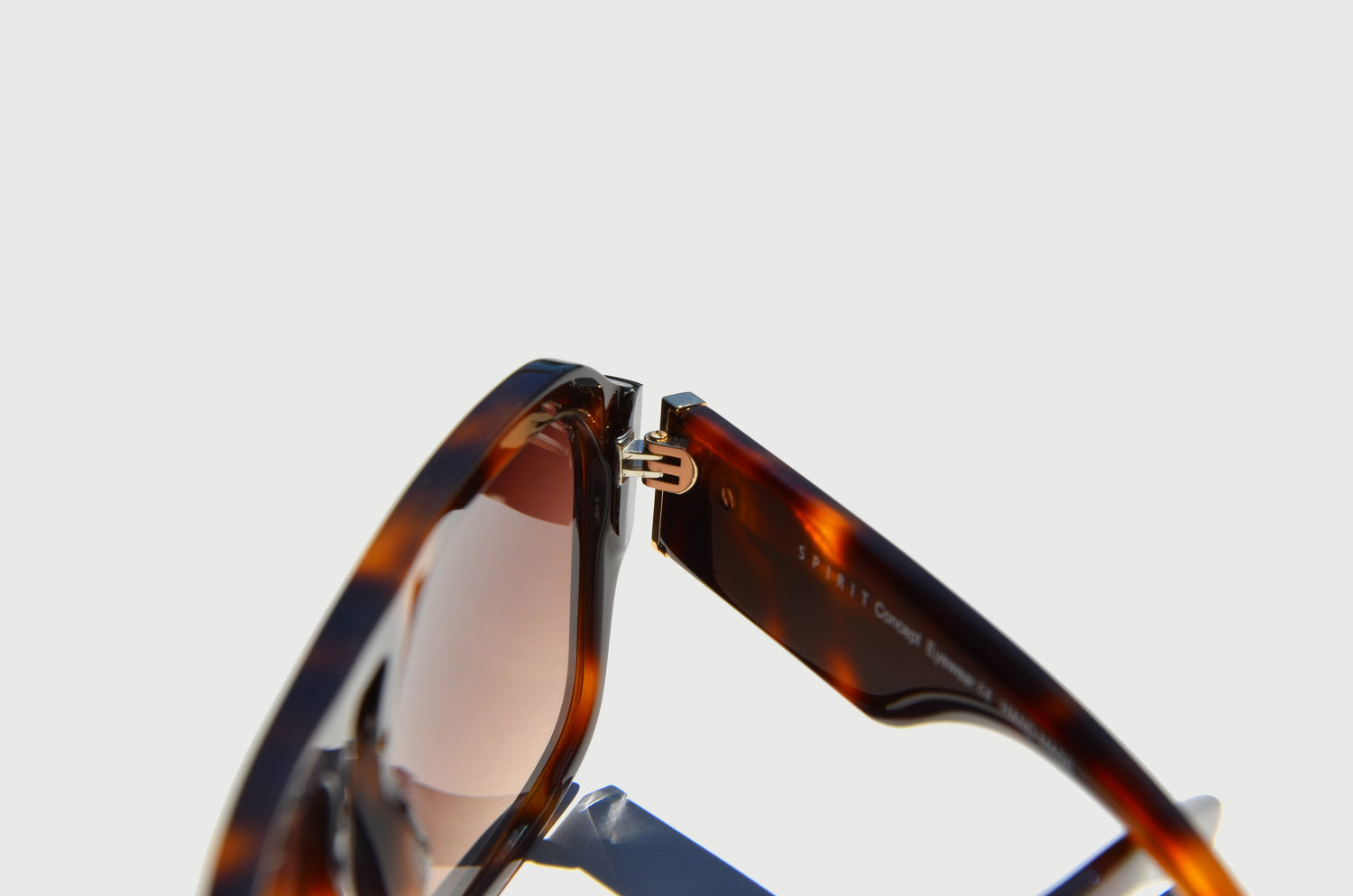 Brown sunglass close up of stainless steel gold hinge with arm slightly folded 