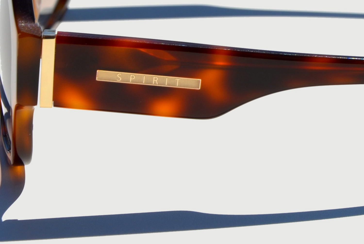 Thick temple of brown sunglasses zoomed in on Spirit gold emblem on side.