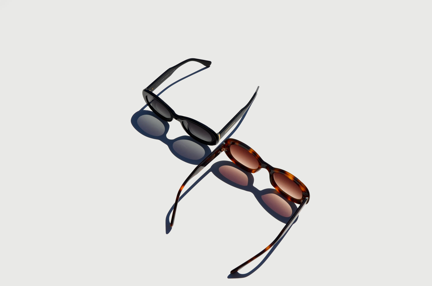 Two pairs of round sunglasses, black brown lenses, angle with their shadows on the surface.