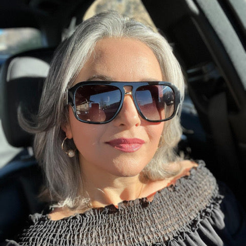 Older woman in car wearing black designer eyewear for generous coverage.