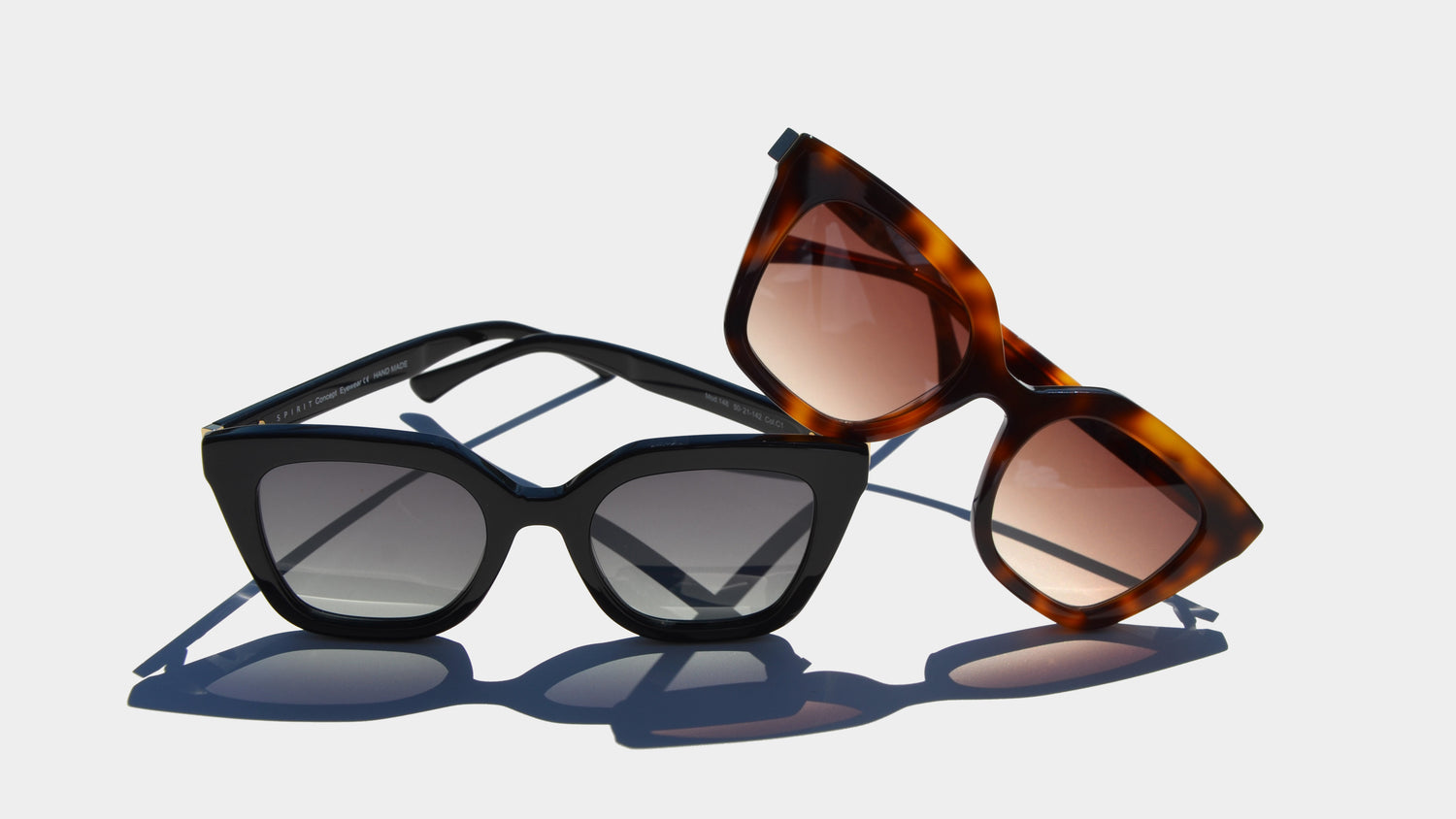 A captivating display of two pairs of cat-eye eyewear resting on a light background. The black eyewear features bold frames with gray-tinted lenses, positioned in the foreground. Behind it, the Havana brown frames, with warm amber lenses, leans at an angle, adding a touch of elegance and depth.