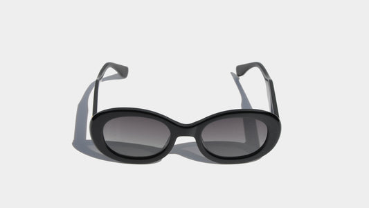 Front view of shiny black oval sunglasses with a sophisticated slim frame design and gradient grey lenses for a modern look.