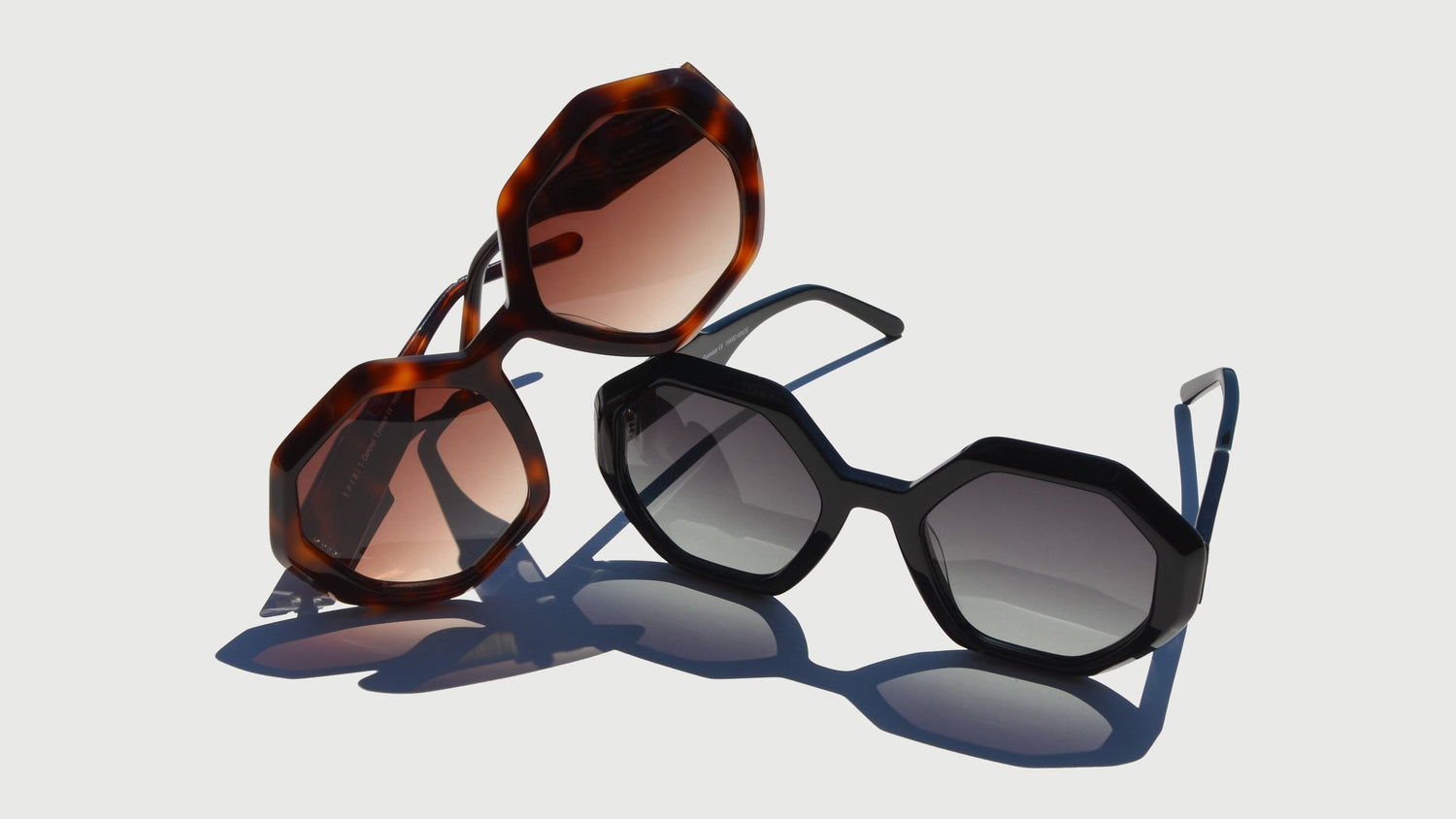 A sophisticated showcase of geometric eyewear featuring bold designs. The Havana pair on the left displays a brown frame with warm amber-tinted lenses, angled dynamically to highlight its octagonal shape. The black pair on the right features gradient gray lenses with sharp geometric edges, set upright.