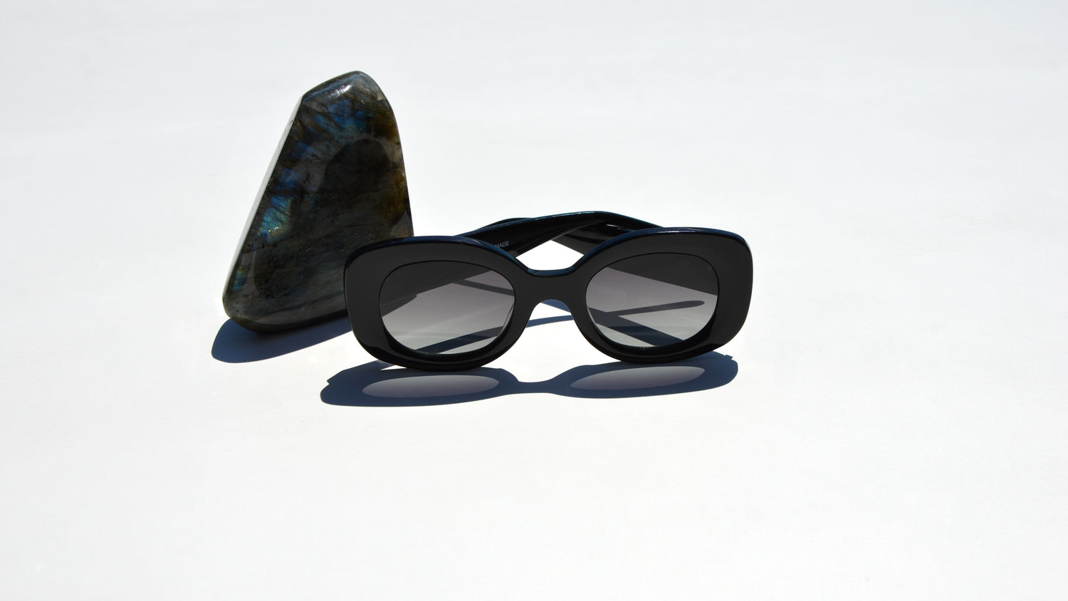 Black bold rounded cat eye sunglasses next to shiny triangular black rock 