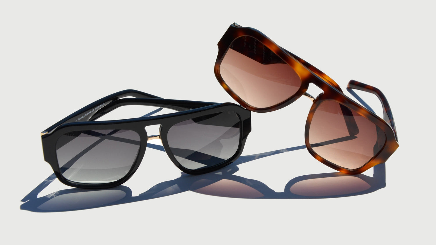 A product image showcasing two navigator style eyewear pairs against a light background. One features a sleek black frame with gradient gray lenses, and the other showcases a Havana tortoise frame with warm amber lenses.