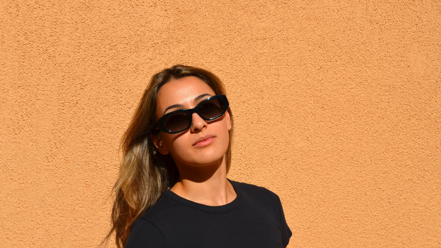 woman wearing black rectangle eyewear black shirt against peach and yellow wall.